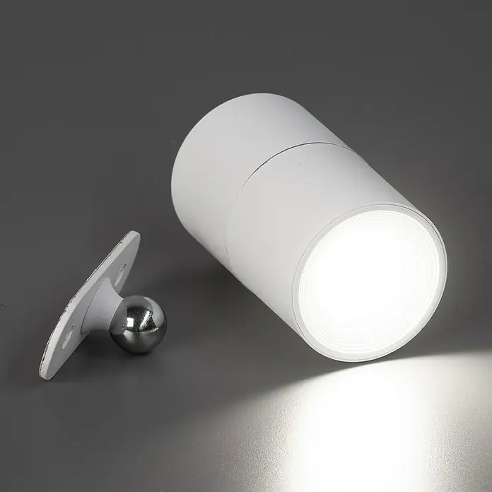 FHL easy Magnetic Akku-Wandleuchte - 9,5 x 5,5 x 5,5 cm, Sandweiß, 1,5 W, IP54, Warmweiß - Weißer zylindrischer Strahler, beleuchtet, mit separater silberner Kugelgelenkhalterung mit weißer Platte.