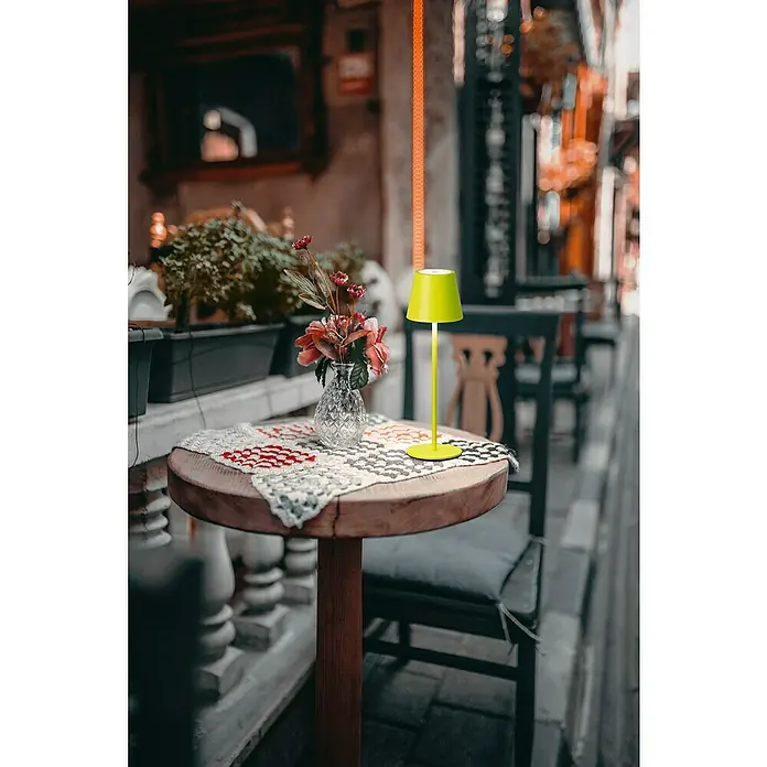 FHL easy Akku-Tischleuchte Viletto - 2 W, L x B x H: 11 x 11 x 36,5 cm, Hellgrün, Warmweiß - Eine hellgrüne, tragbare Tischlampe beleuchtet einen Cafétisch mit Blumen.