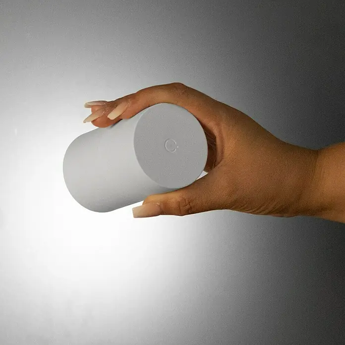 FHL easy Magnetic Akku-Wandleuchte - 9,5 x 5,5 x 5,5 cm, Sandweiß, 1,5 W, IP54, Warmweiß - Hellgraues zylindrisches Objekt, von einer Hand gehalten.