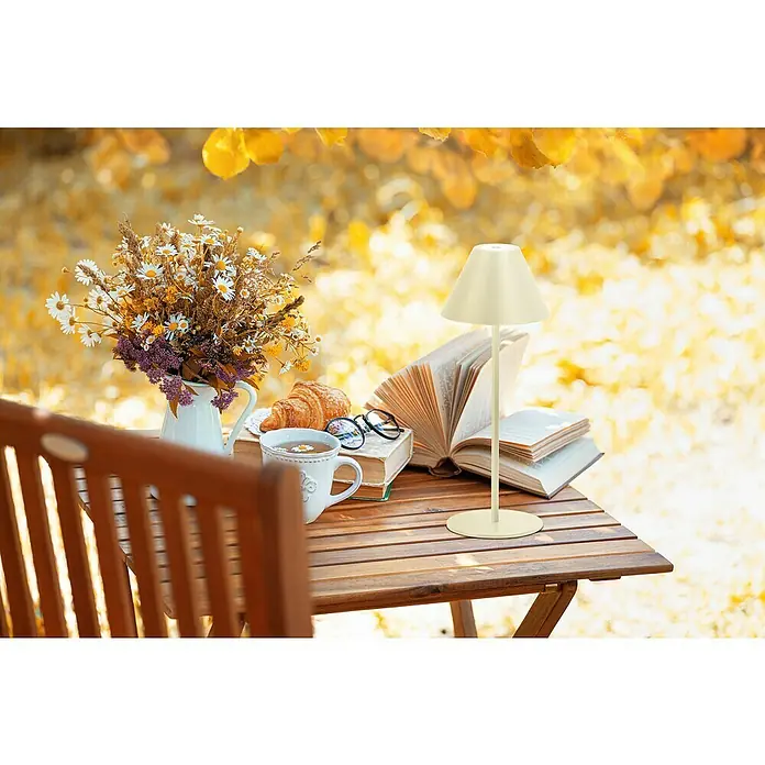 FHL easy Akku-Tischleuchte Kano - 2 W, L x B x H: 14 x 14 x 36 cm, Sand, Warmweiß - Cremefarbene tragbare Tischlampe auf einem Holztisch, inmitten von Büchern, Tee und Herbstlaub.