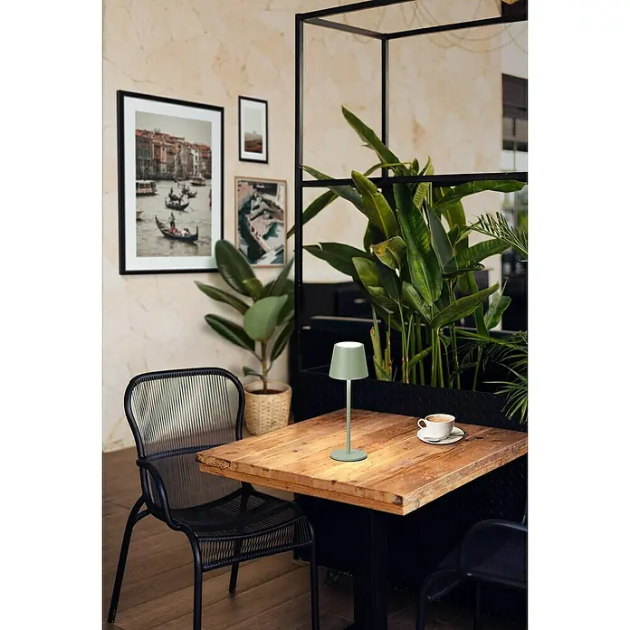 FHL easy Akku-Tischleuchte Roxi - 1,5 W, L x B x H: 9 x 9 x 27,5 cm, Grün, Warmweiß - Salbeigrüner Tischlampe auf rustikalem Holztisch, neben einer weißen Kaffeetasse im Café.