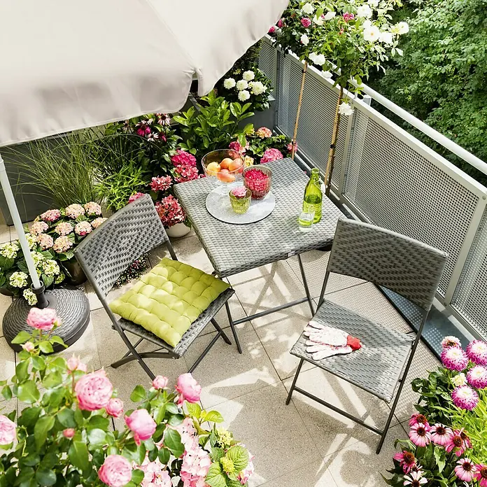 Sunfun Balkonschirm rund Provence II - Natur, Durchmesser Bespannung: 250 cm - Balkon mit grauem Rattantisch und Stühlen umgeben von üppigen Blumen. Der Tisch ist mit Getränken und Obstschalen gedeckt.