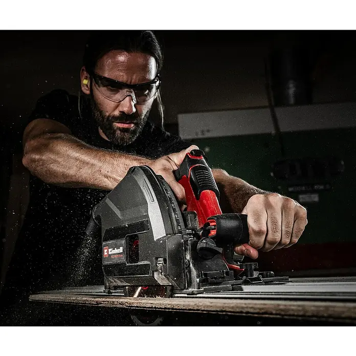Einhell Professional Power X-Change 18V Akku-Tauchsäge TP-PS 18/165 LI BL-Solo - 18 V, Leerlaufdrehzahl: 5.000 U/min - Mann schneidet Holz mit einer rot-schwarzen Einhell Handkreissäge, Späne und Funken fliegen.