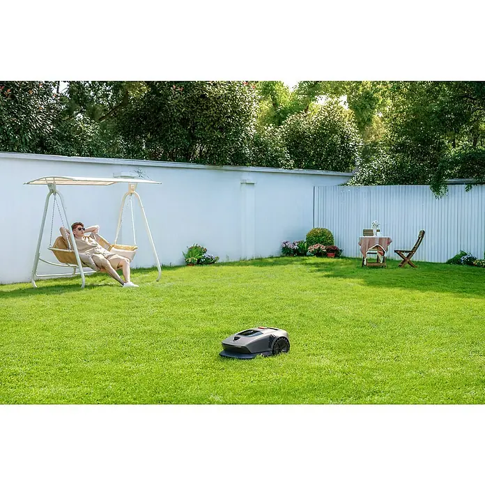 Mova Mähroboter 600 Plus - 600 m², Schnittbreite: 20 cm, Laser-gestützte Navigation, LiDAR - Ein Rasenmähroboter pflegt den Rasen, während ein Mann in einer Schaukel entspannt. Praktische Gartenarbeit mit moderner Technologie.