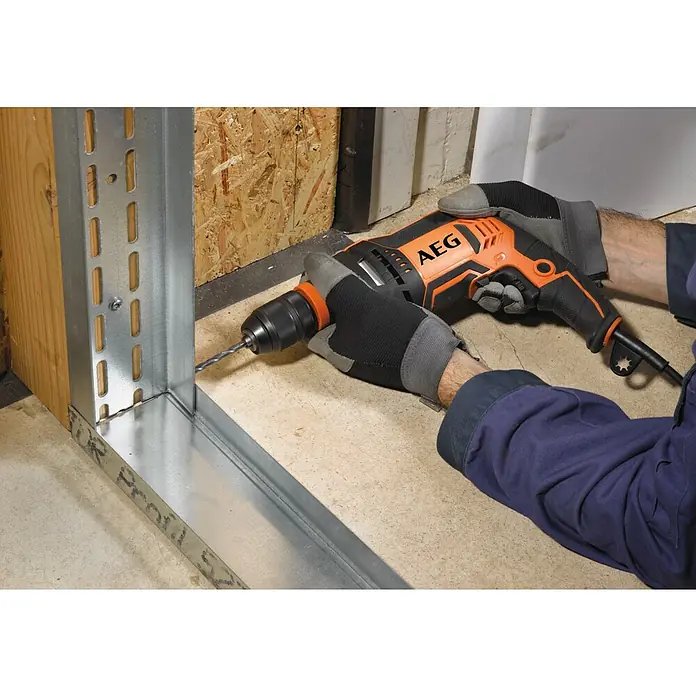 AEG Schlagbohrmaschine SBE 750 RE - 750 W, Schnellspannbohrfutter - Ein Arbeiter in Handschuhen bohrt mit einer orange-schwarzen AEG Bohrmaschine in ein Metallprofil, um eine Konstruktion zu montieren.