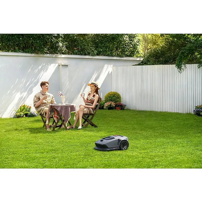 Mova Mähroboter 600 Plus - 600 m², Schnittbreite: 20 cm, Laser-gestützte Navigation, LiDAR - Ein Rasenmähroboter mäht den Rasen, während ein Paar Kaffee im Garten genießt. Der Fokus liegt auf dem modernen Rasenmäher.