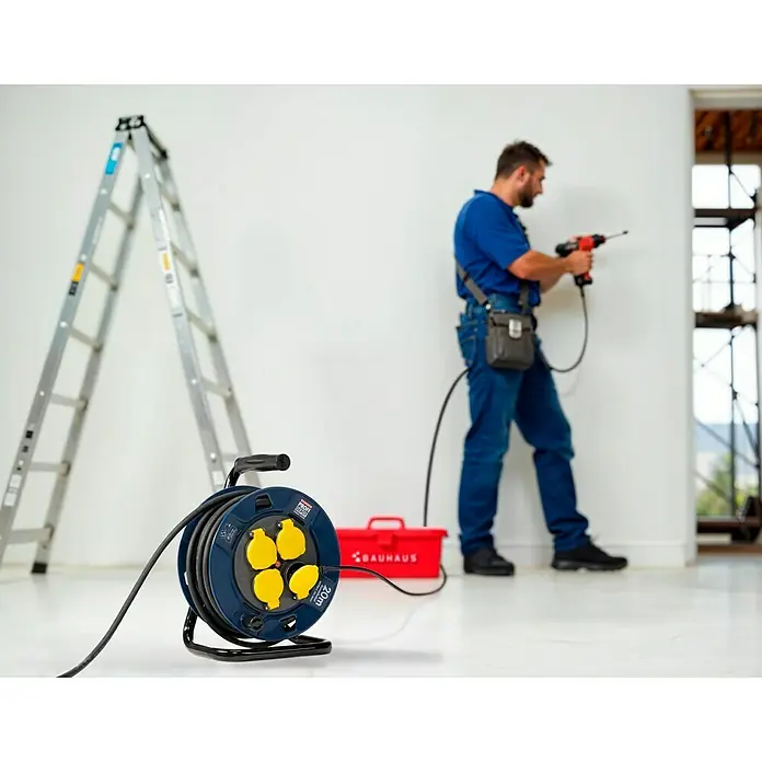 Profi Depot Kabeltrommel - Kunststoff, 20 m, H07RN-F, IP44 - Eine blaue Bauhaus-Kabeltrommel mit gelben Steckdosen, neben einer Leiter und einem Arbeiter mit Bohrmaschine.