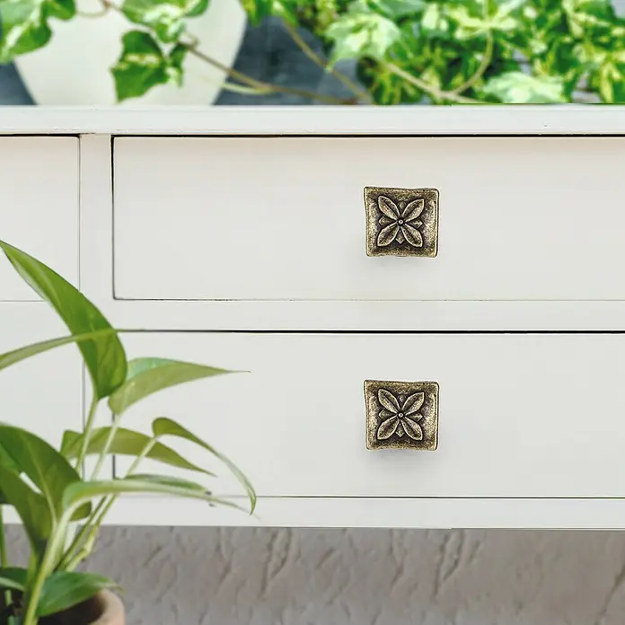 Rei Pomo para muebles - L x An: 33 x 33 mm, Cuero viejo, 4 ud. - Detalle de dos cajones blancos con pomos de latón cuadrados con motivos florales y plantas verdes al fondo.