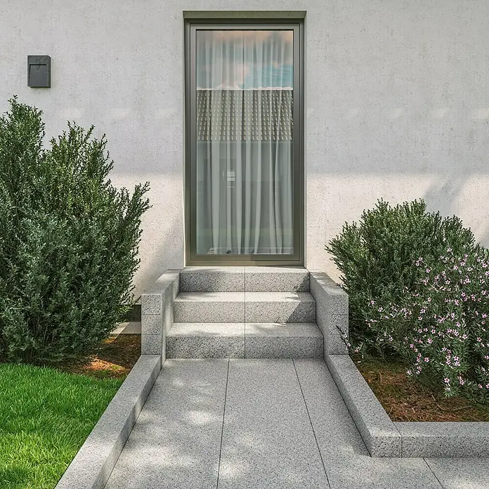 Granitstufe G 603 - Grau, 50 x 33 x 15 cm - Eingangsbereich mit modernem Fenster, umgeben von üppigem Grün und stilvollem Steindesign. Das Fenster lässt viel Licht herein.
