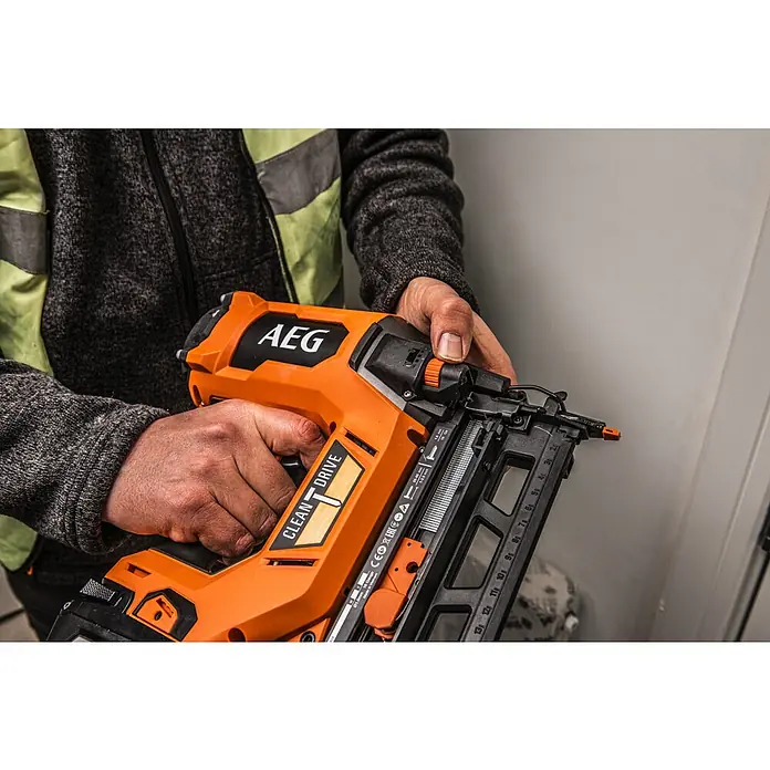 AEG Pro 18V Akku-Nagler B18BN16-0 - 18 V, Ohne Akku, Länge Nagel: 25 mm - 65 mm - Eine Person hält eine orange-schwarze AEG Nagelpistole mit 'CLEAN DRIVE'-Technologie, deren 16-Gauge Nagelmagazin sichtbar ist.