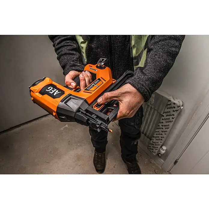 AEG Pro 18V Akku-Nagler B18BN16-0 - 18 V, Ohne Akku, Länge Nagel: 25 mm - 65 mm - Person hält ein orange-schwarzes AEG Nagler, bereit für Befestigungsarbeiten.
