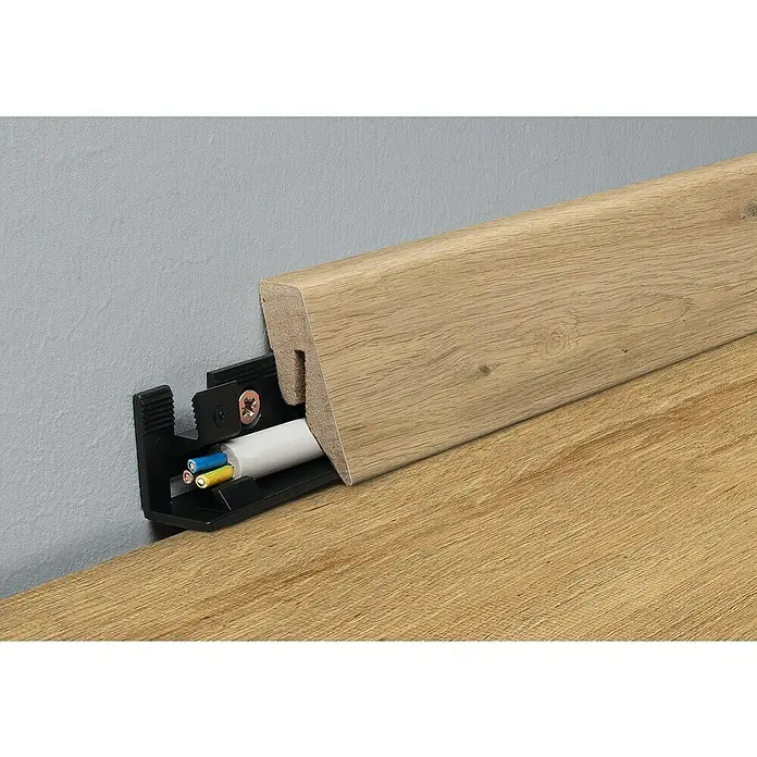 LOGOCLIC Sockelleiste Sixtyfive - 260 cm x 19 mm x 40 mm, MDF - Eine Sockelleiste mit Kabelkanal in Holzoptik ist an einer grauen Wand und einem hölzernen Boden befestigt, um Kabel ordentlich zu verstauen.