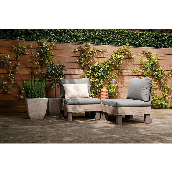 Keter Elements Respaldo de respaldo con cojín - L x An x Al: 60 x 17 x 57 cm, Madera/Verde - Dos sillones de salón grises con marcos de madera clara se sientan en una cubierta de madera frente a una pared de madera con plantas trepadoras.