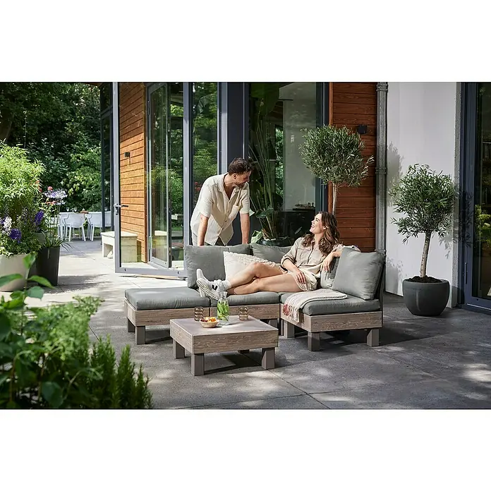 Keter Elements Respaldo de respaldo con cojín - L x An x Al: 60 x 17 x 57 cm, Madera/Verde - Una pareja relajada disfruta de un juego de salón modular de exterior con mesa de centro en una elegante terraza verde.