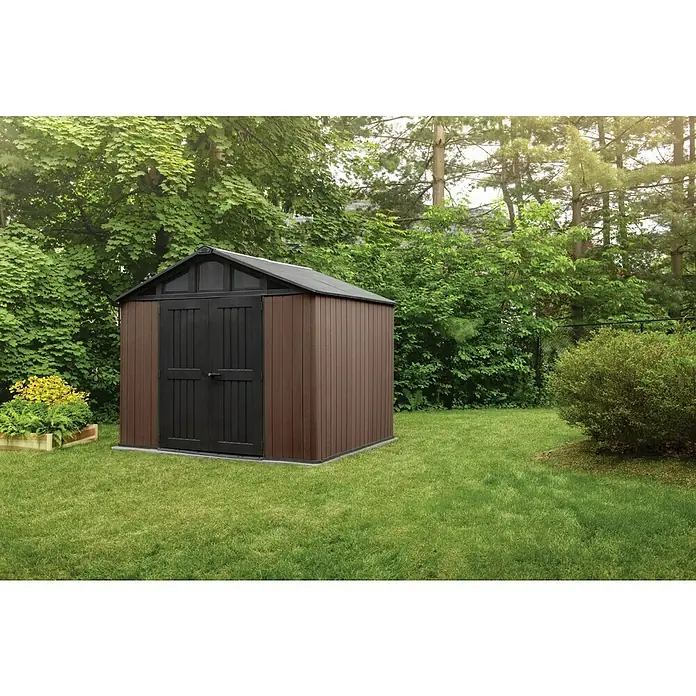 Keter Caseta de jardín Stronghold 2.0 - Medidas ext. (An x Pr): 305 x 243 cm, Plástico, Marrón/Negro, 7,4 m² - Un cobertizo de herramientas marrón con un techo a dos aguas negro se alza sobre una pradera verde rodeada de árboles. El foco está en el cobertizo espacioso.