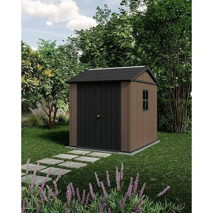 Keter Caseta de jardín Newton Plus 757-775 - Medidas ext. (An x Pr): 223 x 230 cm, Plástico, Marrón/Negro, 4,4 m² - Una caseta de jardín marrón con techo negro y puertas negras en el verde. Delante, hay piedras y flores moradas.