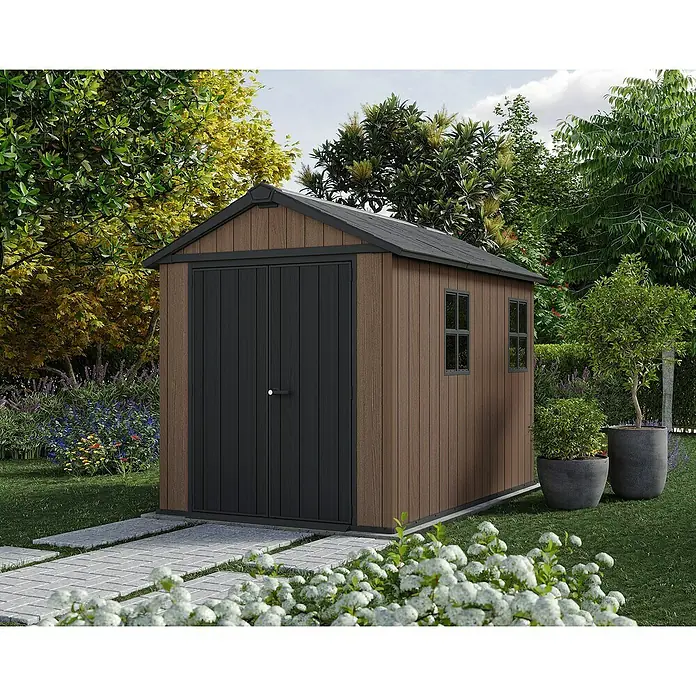 Keter Caseta de jardín Newton Plus 759-975 - Medidas ext. (An x Pr): 287 x 230 cm, Plástico, Marrón/Negro, 5,25 m² - Una caseta de jardín marrón con puertas oscuras y marcos de ventanas se encuentra en el jardín. El jardín es exuberante con plantas y vegetación.