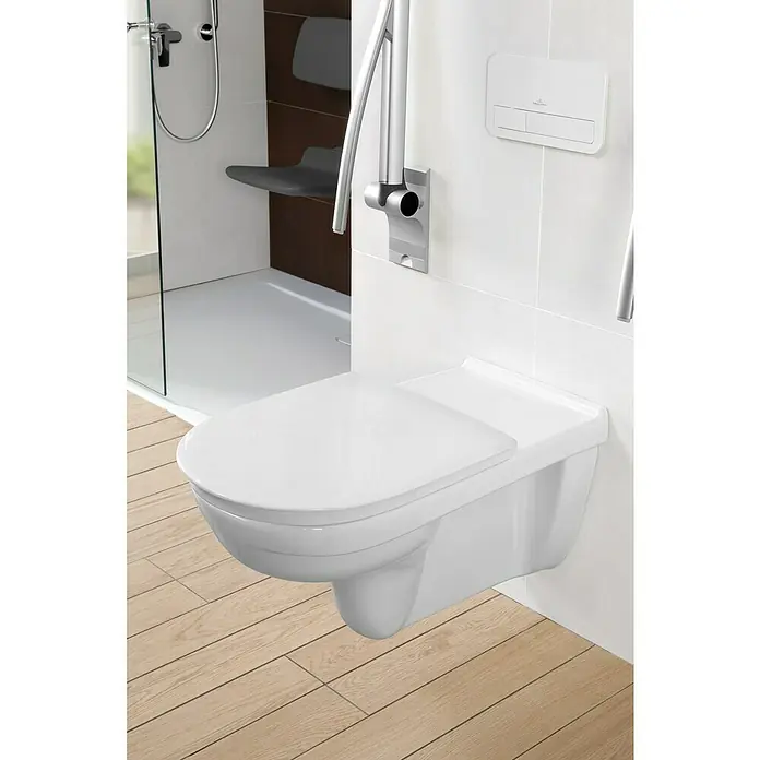 Villeroy & Boch ViCare WC-Sitz - Duroplast, Weiß, Mit Absenkautomatik - Nahaufnahme einer Villeroy & Boch Wandtoilette mit Haltegriff und Duschbereich im Hintergrund für barrierefreies Badezimmerdesign.