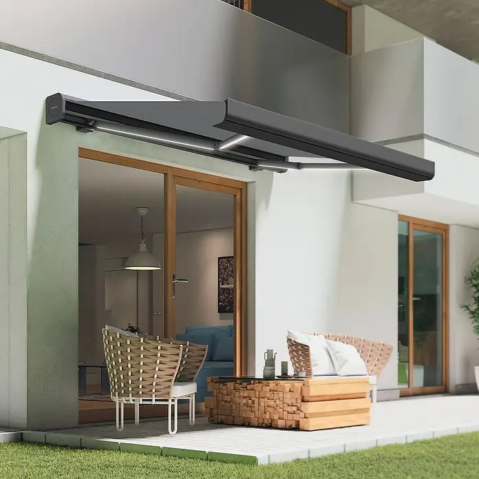 SmartSun Toldo con motor Dark Algarve - Gris, Ancho: 4,75 cm, Caída: 3 m - Toldo retráctil gris con iluminación LED, que proporciona sombra sobre un patio con sillas de ratán y mesa de madera.