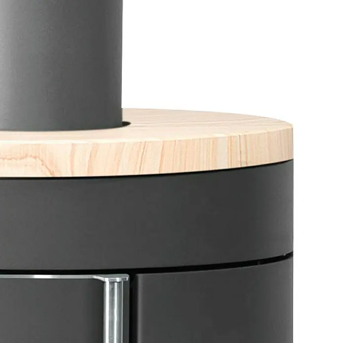 Justus Kaminofen Mino Trios 2.0 - 5,5 kW, Raumheizvermögen: 88 m³, Farbe Verkleidung: Sandstein, Schwarz - Nahaufnahme eines schwarzen Ofens mit einer hellen Holzplatte oben, die eine moderne und stilvolle Heizlösung zeigt.