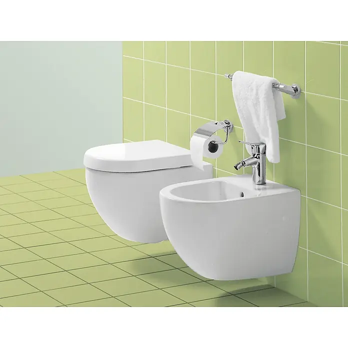 Villeroy & Boch Subway WC-Sitz Compact - Duroplast, Weiß, Mit Absenkautomatik - Das Bild zeigt eine moderne Toilette und ein Bidet in einem Badezimmer mit grünen Fliesen, die ein sauberes und stilvolles Ambiente schaffen.