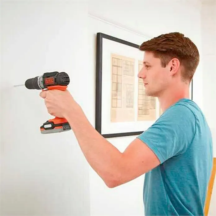 Black+Decker Taladro atornillador percutor de batería BDCHD12S1-XJ - 12 V, 1 batería, 40 Nm - Un hombre taladra un agujero en una pared blanca con un taladro inalámbrico Black+Decker.