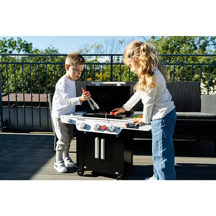 Klein Kinder-Grill Weber Genesis - L x B x H: 740 x 328 x 597 mm - Zwei Kinder spielen mit einem Genesis-Spielzeuggrill im Freien, wobei das realistische Design und die interaktiven Funktionen im Vordergrund stehen.