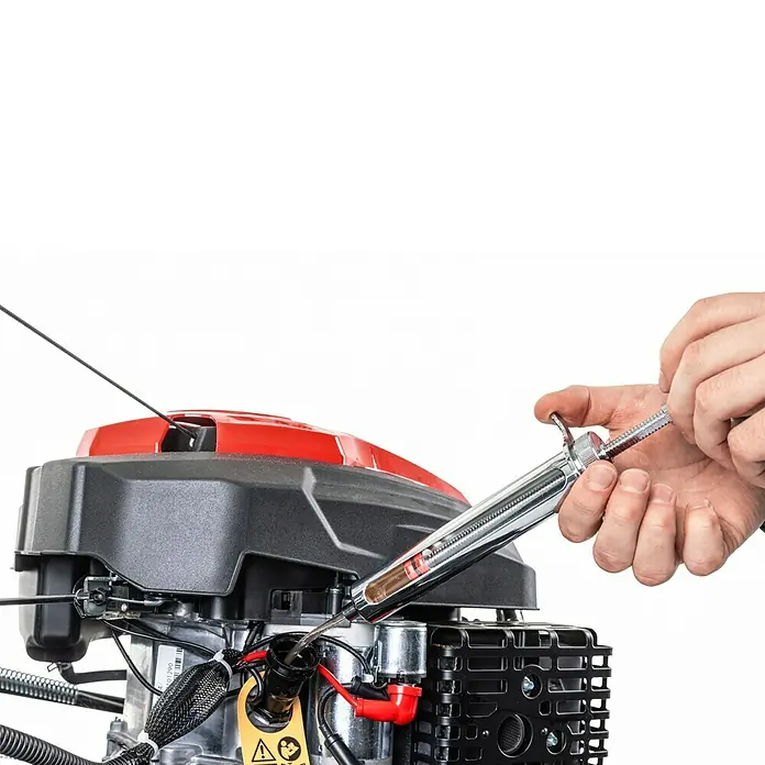 Scheppach Wartungs-Kit für Rasenmäher - 4-Takt-Benzin Geräte, 5 -tlg. - Hand füllt Öl mit einer Metallspritze in einen Kleinmotor mit roter Abdeckung.