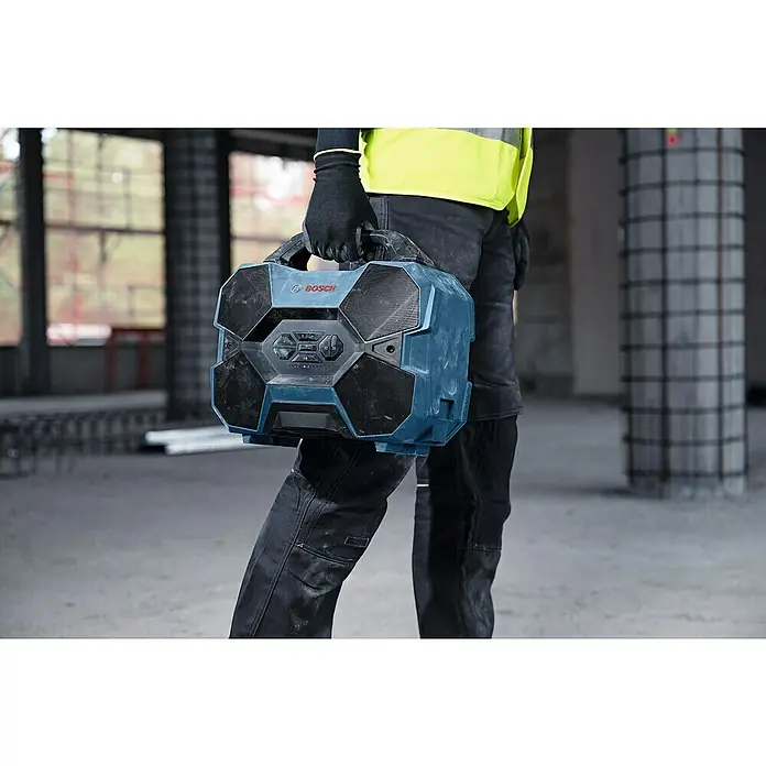 Bosch Professional AMPShare 18V Bluetooth-Lautsprecher GPB 18V-6 C - 18 V, Ohne Akku - Blauer und schwarzer robuster Bosch Baustellenradio mit Lautsprechern und Bedienelementen, von einem Arbeiter auf einer Baustelle getragen.