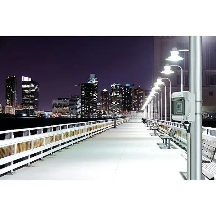 Hensel  Aufputz-Verteiler KV9103 - Anzahl Reihen: 1 Stk., 10,2 x 19,7 cm, Grau - Bild einer langen Seebrücke bei Nacht mit Blick auf die Lichter der Stadt und einem Verteilerkasten von Fibox auf einem Poller.