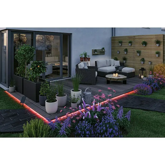 Paulmann LED-Band-Set Stripe Solar - 10 m, RGB, 3,8 W, 300 lm, 5 V - Stimmungsvolle Gartengestaltung mit LED-Beleuchtung, Pflanzkübeln und gemütlicher Sitzecke auf einer Holzterrasse mit blühenden Blumen.