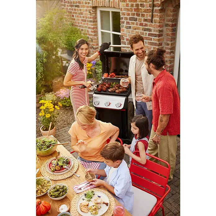 Weber Gasgrill Spirit E-310 - Grillfläche (B x T): 52 x 44 cm, 7 kW, Anzahl Brenner: 3 Stk. - Eine Gruppe von Menschen grillt und isst im Freien, mit einem Spirit Grill im Mittelpunkt.