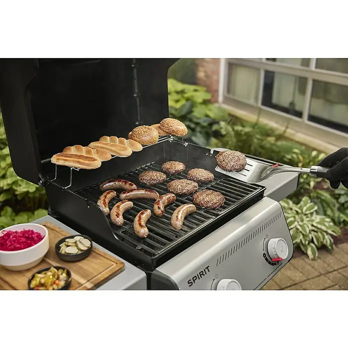 Weber Gasgrill Spirit E-210 - Grillfläche (B x T): 52 x 44 cm, 7,8 kW, Anzahl Brenner: 2 Stk. - Bild eines Weber Spirit Grills mit Burgern, Würstchen und Brötchen, der die Vielseitigkeit und Möglichkeiten des Grills hervorhebt.