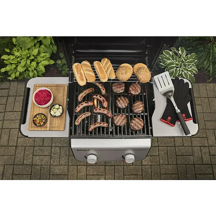 Weber Gasgrill Spirit E-210 - Grillfläche (B x T): 52 x 44 cm, 7,8 kW, Anzahl Brenner: 2 Stk. - Ein Weber Gasgrill mit Würstchen, Burgern und Brötchen, dazu Beilagen wie Krautsalat und eingelegte Gurken, bereit für ein leckeres Barbecue.