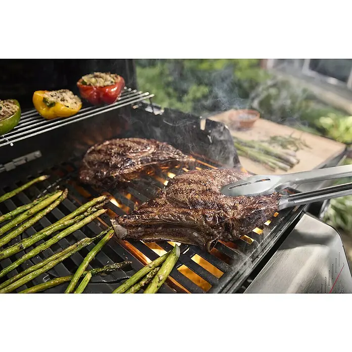 Weber Gasgrill Spirit E-310 - Grillfläche (B x T): 52 x 44 cm, 7 kW, Anzahl Brenner: 3 Stk. - Grill mit zwei Steaks, gefüllten Paprika und Spargel. Eine Grillzange wendet das Fleisch auf dem heißen Grill.