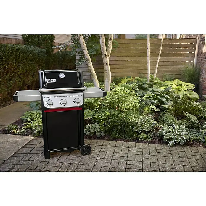 Weber Gasgrill Spirit E-310 - Grillfläche (B x T): 52 x 44 cm, 7 kW, Anzahl Brenner: 3 Stk. - Nahaufnahme eines Weber Spirit Gasgrills mit drei Brennern auf einer Terrasse mit üppigem Grün.