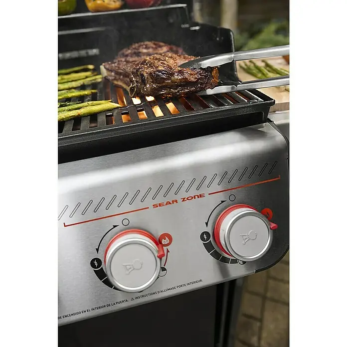 Weber Gasgrill Spirit E-335 GBS - Grillfläche (B x T): 52 x 44 cm, 9,1 kW, Anzahl Brenner: 3 Stk. - Nahaufnahme eines Grills mit einem saftigen Steak und Spargel, der mit einer Zange gewendet wird, im Fokus.