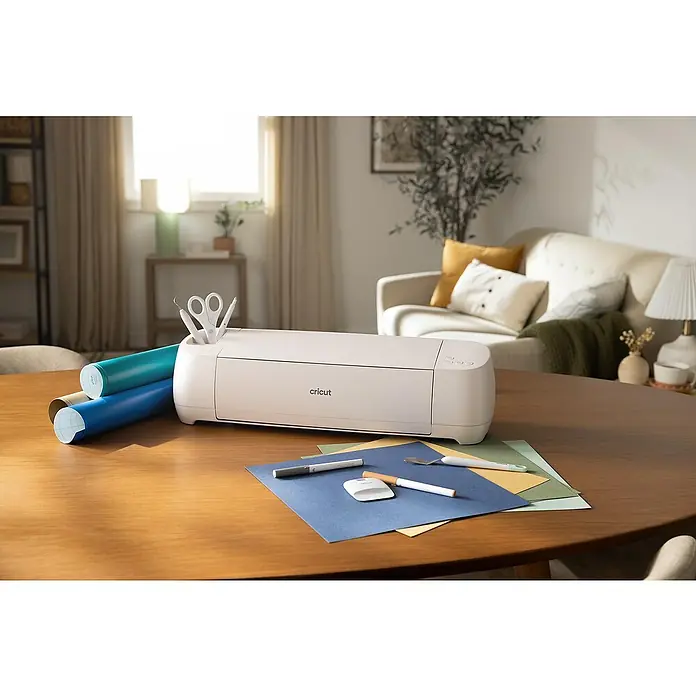 Cricut Maker Plotter de corte Maker 4 Essentials-Bundle - Gris/ Verde, Bluetooth, Ancho de corte: 29,7 cm, Longitud de corte: 3,6 m - Primer plano de una máquina de corte Cricut sobre una mesa de madera, rodeada de materiales para manualidades.