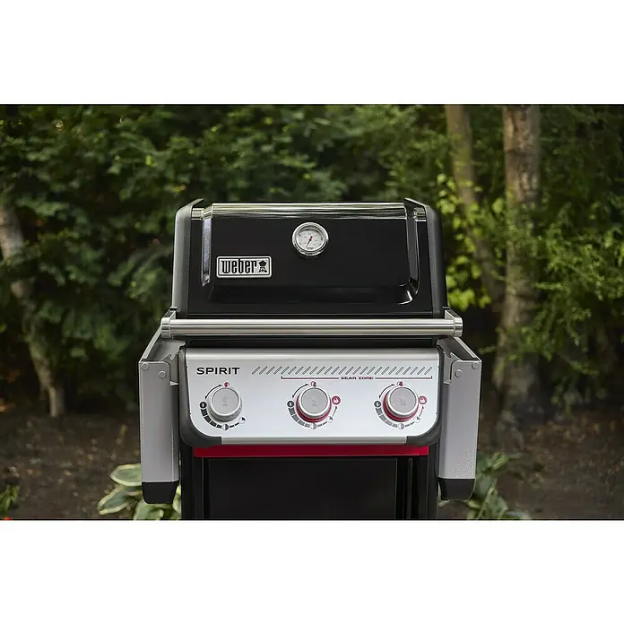 Weber Gasgrill Spirit E-325 GBS - Grillfläche (B x T): 52 x 44 cm, 9,1 kW, Anzahl Brenner: 3 Stk. - Nahaufnahme eines Weber Spirit Gasgrills im Außenbereich, der die Bedienelemente und das Thermometer hervorhebt.