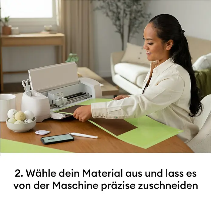 Cricut Maker Plotter de corte Maker 4 Essentials-Bundle - Gris/ Verde, Bluetooth, Ancho de corte: 29,7 cm, Longitud de corte: 3,6 m - Una mujer carga material marrón sobre una alfombrilla verde en una máquina de corte blanca para un corte preciso.