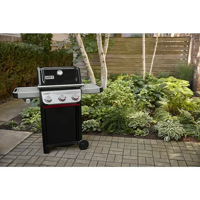 Weber Gasgrill Spirit E-335 GBS - Grillfläche (B x T): 52 x 44 cm, 9,1 kW, Anzahl Brenner: 3 Stk. - Ein Weber Spirit II Gasgrill steht auf einer gepflasterten Terrasse, umgeben von üppigem Grün, bereit für das nächste Grillfest.