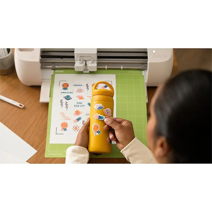 Cricut Plotter de corte Explore 4 - Blanco, Bluetooth, Ancho de corte: 29,7 cm, Longitud de corte: 3,6 m - Una mujer está aplicando pegatinas de colores a una botella de agua amarilla, con una máquina de corte Cricut Maker 3 en una mesa a su lado.