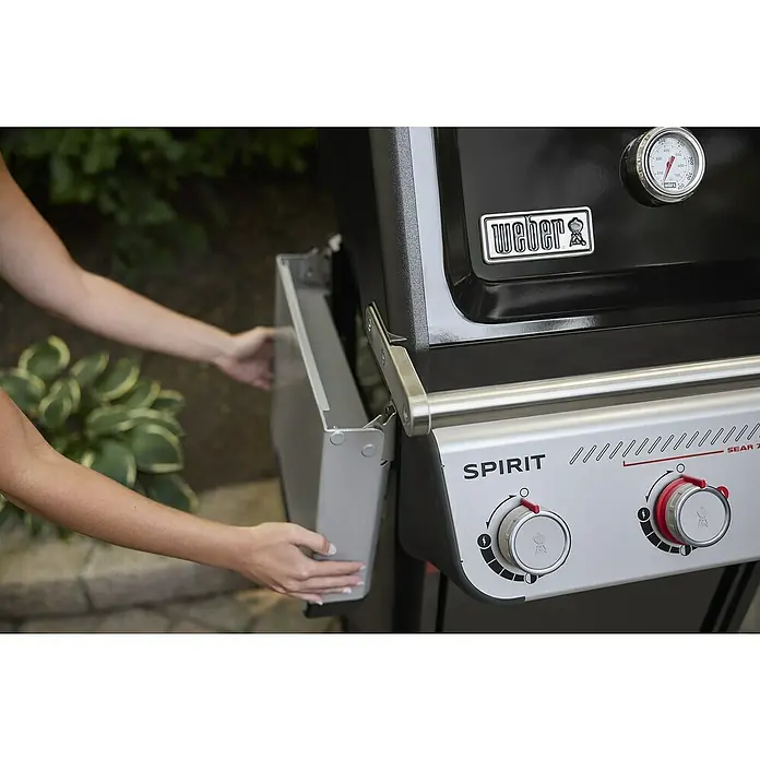 Weber Gasgrill Spirit E-425 GBS - Grillfläche (B x T): 62 x 44 cm, 10,3 kW, Anzahl Brenner: 4 Stk. - Detailaufnahme eines Weber Spirit Sear 2-Brenner Gasgrills mit Seitentisch, der von einer Person bedient wird.