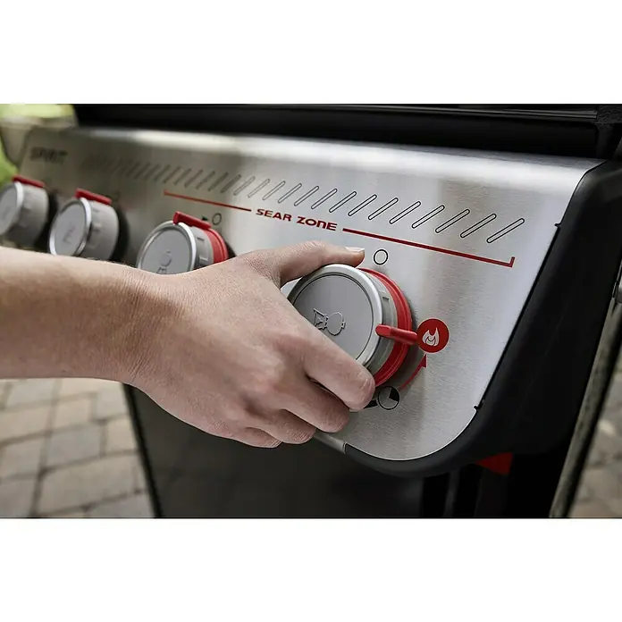 Weber Gasgrill Spirit E-425 GBS - Grillfläche (B x T): 62 x 44 cm, 10,3 kW, Anzahl Brenner: 4 Stk. - Nahaufnahme eines Weber Spirit Sear Zone Grills, der von einer Hand bedient wird. Hervorhebung der Bedienelemente und des Sear Zone Designs.