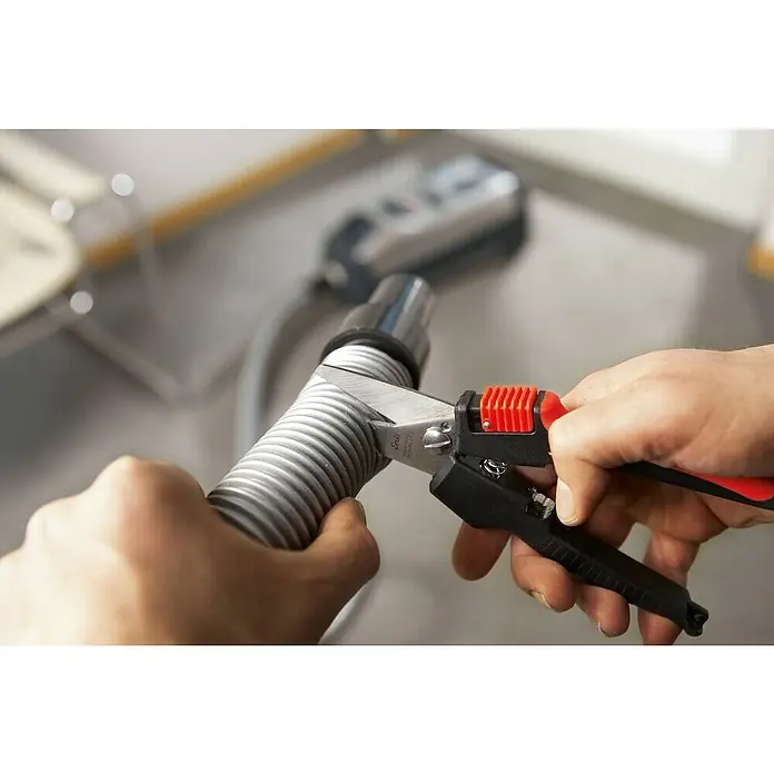 Bessey Tijera universal multiusos Combinox - Largo: 190 mm, Longitud de corte: 40 mm, Acero inoxidable, Negro/Rojo - Una persona corta una manguera de aspiradora gris con unos corta mangueras. Los corta mangueras tienen un mango rojo para un mejor agarre.