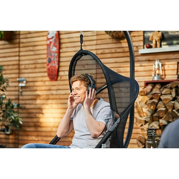 Siena Garden Hängesessel Yobaya mit Schutzhülle - L x B x H: 106 x 123 x 195 cm, Schwarz - Ein Mann sitzt in einem Hängesessel und genießt Musik mit Kopfhörern. Die Hängevorrichtung bietet Komfort und Entspannung im Freien.