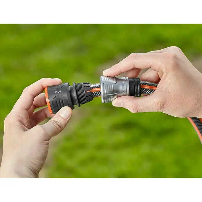 Gardena Schlauchkupplung - Größe: ½″, Mit Wasserstopp - Gartenschlauchverbinder in Aktion. Zwei Hände verbinden einen Schlauch mit einem Gardena-Anschlussstück vor grünem Hintergrund.