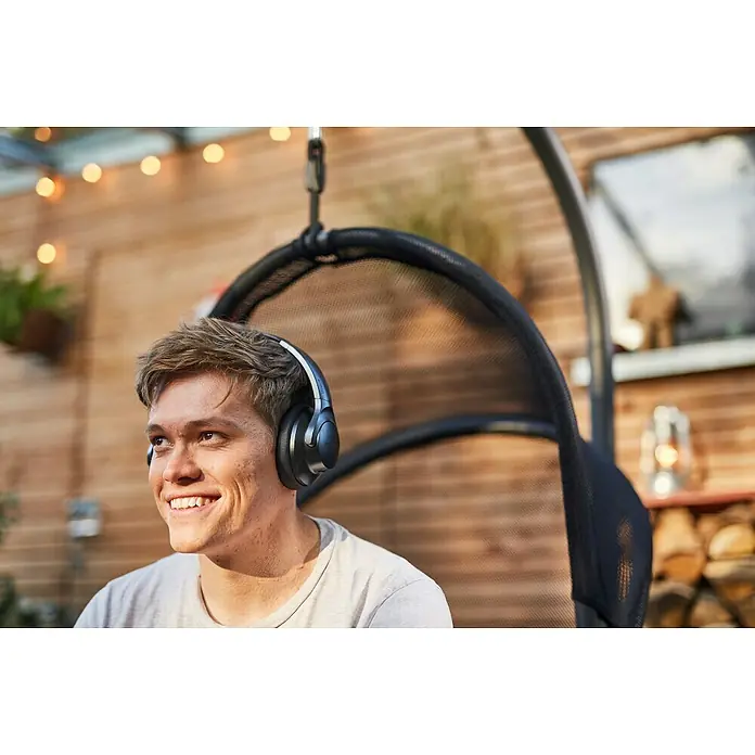Siena Garden Hängesessel Yobaya mit Schutzhülle - L x B x H: 106 x 123 x 195 cm, Schwarz - Ein junger Mann sitzt mit Over-Ear-Kopfhörern in einem Hängesessel und genießt Musik im Freien. Er trägt ein graues T-Shirt und lächelt.