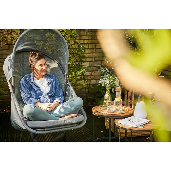 Siena Garden Hängesessel Yobaya mit Schutzhülle - L x B x H: 106 x 123 x 195 cm, Blau - Eine Frau entspannt in einem grauen Hängesessel im Freien mit einem Beistelltisch daneben.