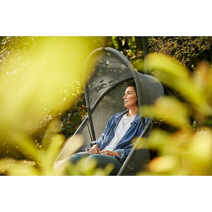 Siena Garden Hängesessel Yobaya mit Schutzhülle - L x B x H: 106 x 123 x 195 cm, Blau - Eine Frau entspannt in einem grauen Hängesessel im Freien, umgeben von üppigem Grün, und genießt die Ruhe und das Sonnenlicht. Der Sessel bietet Komfort und Stil.